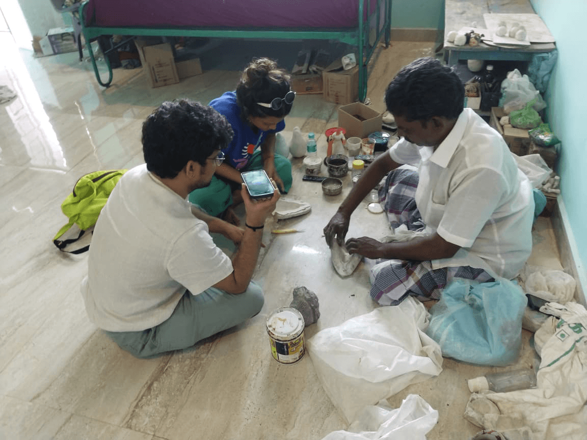Artisan guiding travellers shaping a clay doll by hand