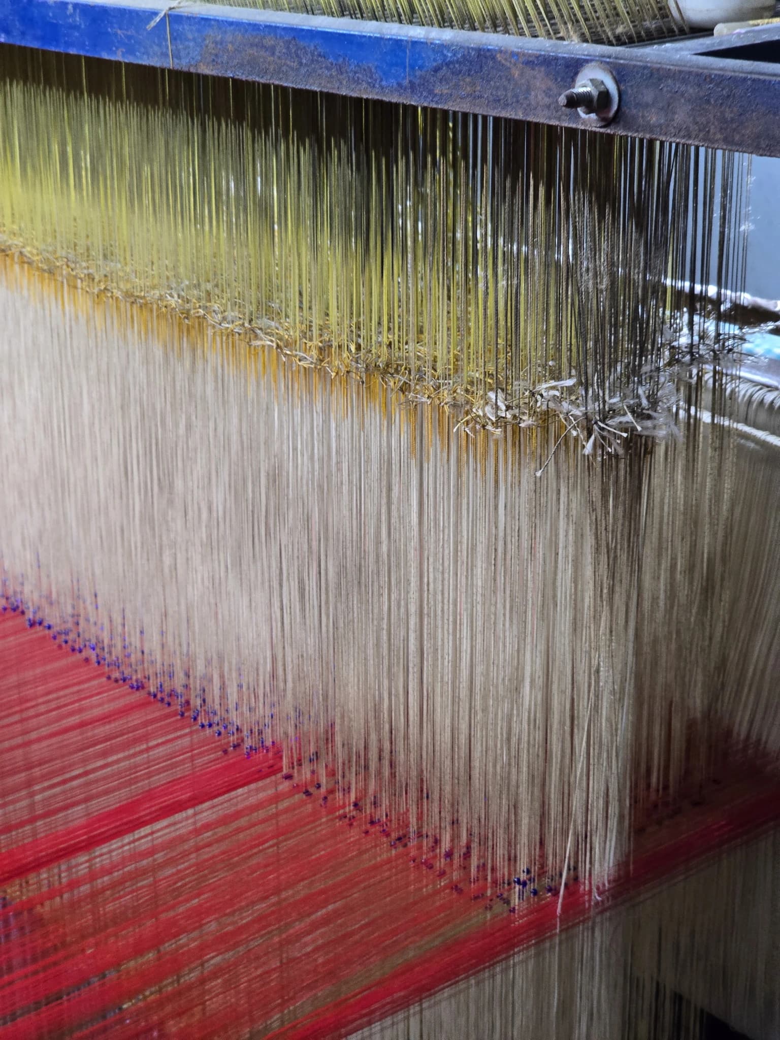 Macro detail of warp threads meeting the woven red silk on the loom